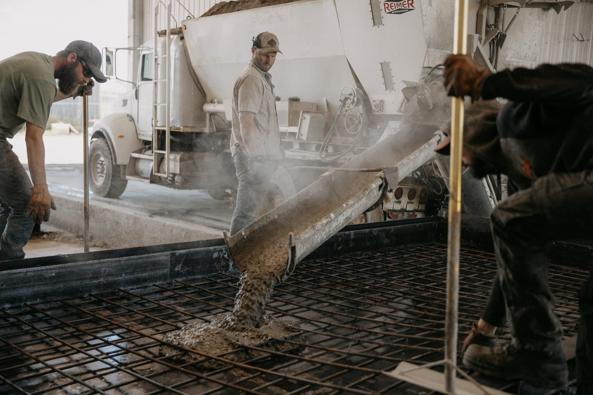 An AltaMix crew pouring concrete from the mixer chute over a rebar grid, dust in the air.